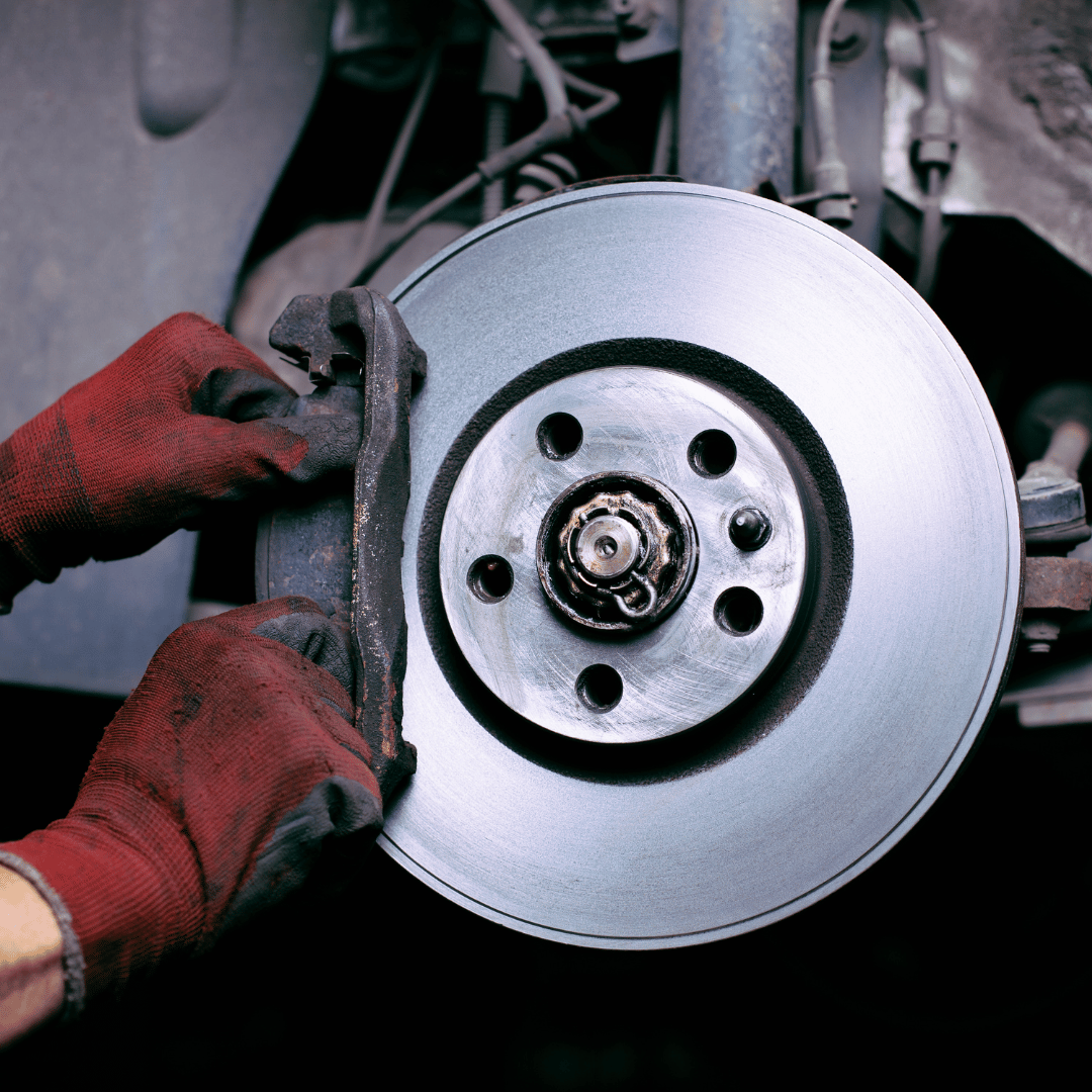 Hands working on automotive brakes: A close-up image featuring a brake rotor and caliper with skilled hands performing maintenance or repairs on the braking system, showcasing expertise and attention to vehicle safety.
